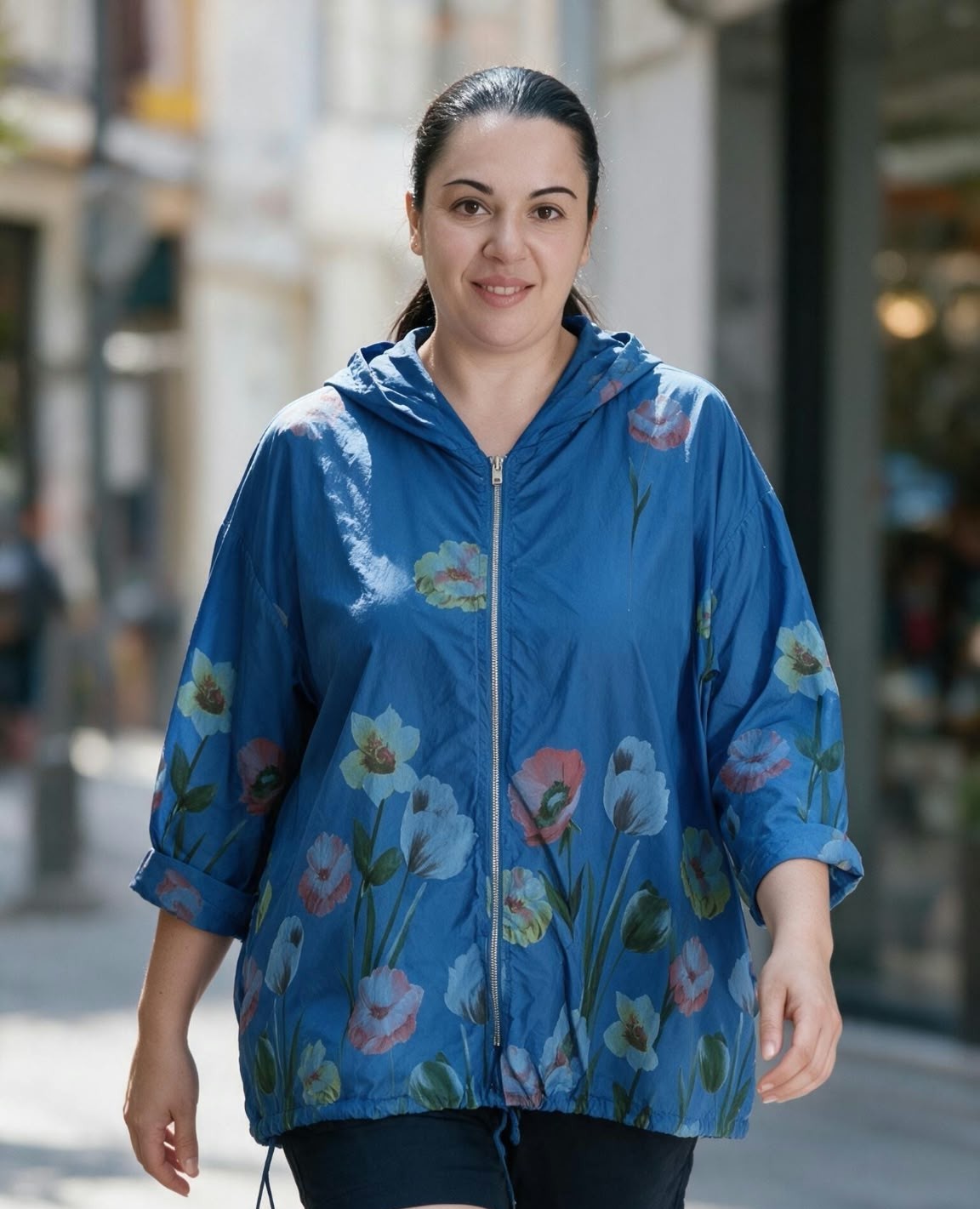 Chaqueta chubasquero ligera de color azul eléctrico con un vistoso estampado de flores y tulipanes en tonos coral, celeste y blanco, equipada con capucha, cierre frontal de cremallera y cordón ajustable en el bajo.